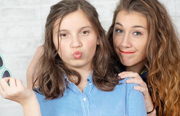 two teen girls, one smiling, the other with puckered lips and sunglasses in her hand